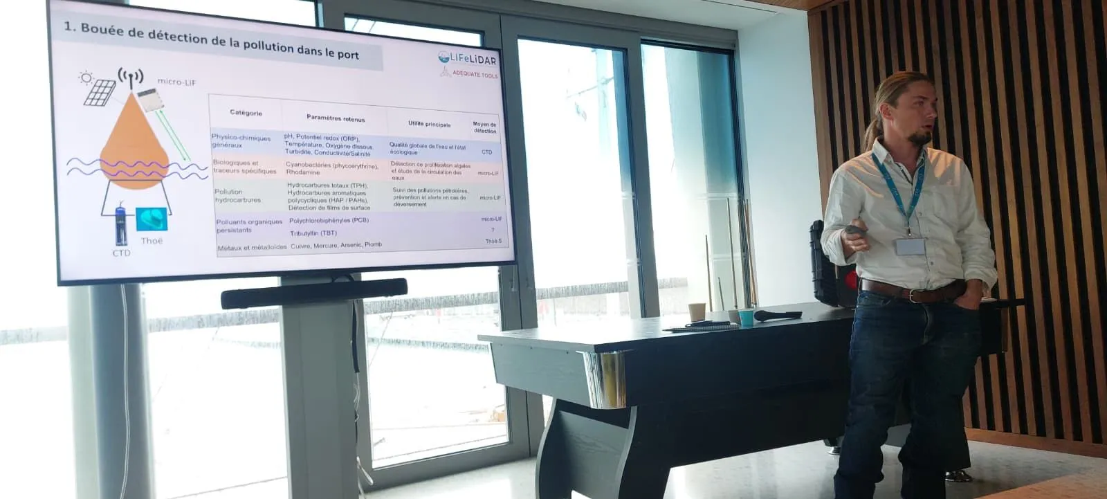 A presenter standing beside a screen that shows the port pollution-detection buoy slide, at Réinventer les Ports d'Antibes