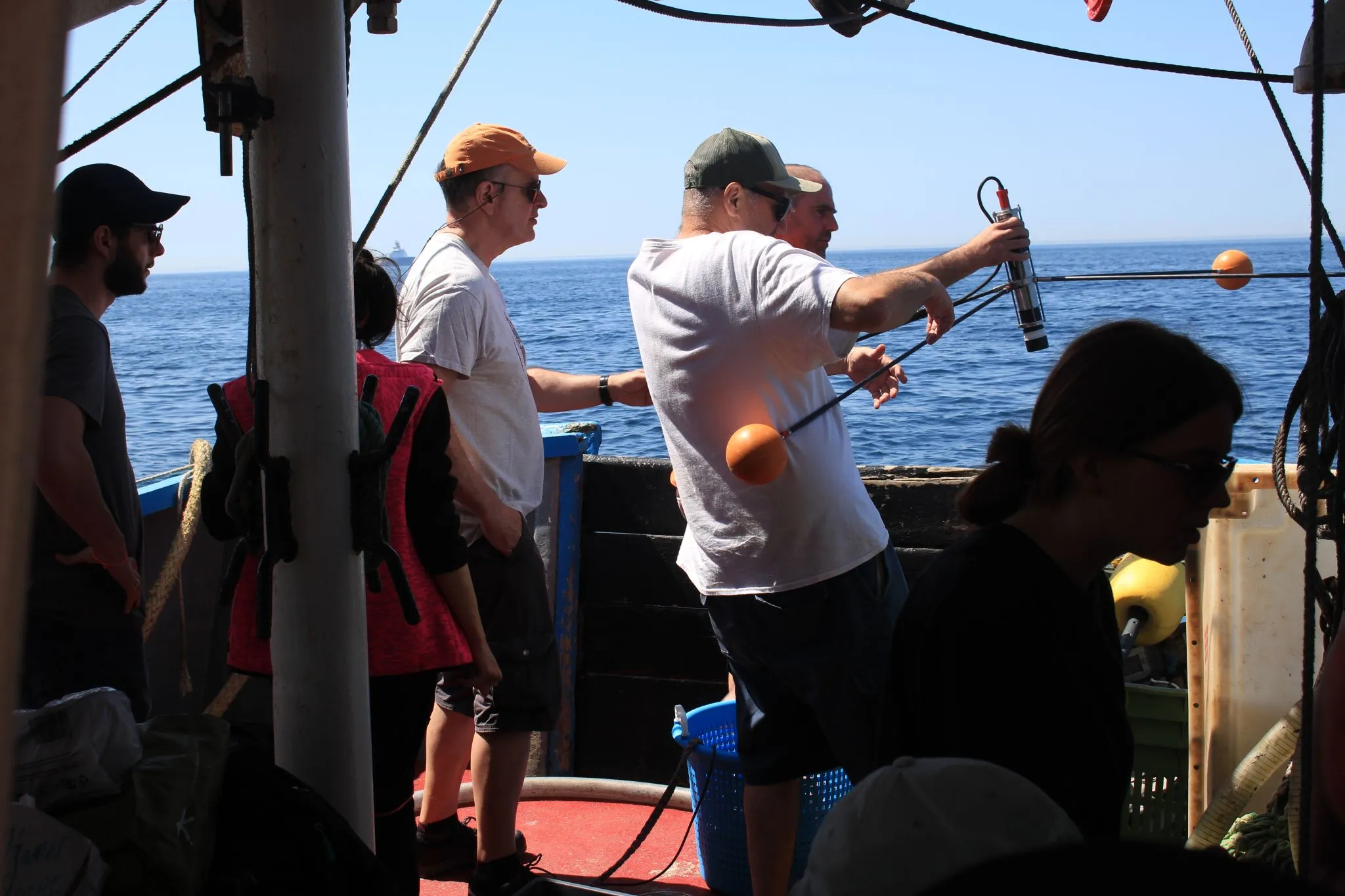 The deck of Sépia II under a clear sky, a crew member lowering a probe on a line over the side, the open Channel behind